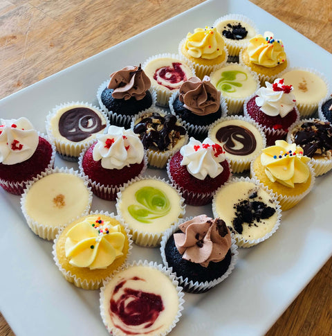 2-bite -sized, Assorted Mini Cheesecakes and Cupcakes arranged on a white platter, for a party.