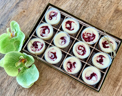 One dozen strawberry swirl cheesecake minis in a gift box, sitting on a table