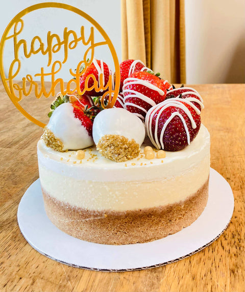 Elegant birthday cheesecake with fresh strawberries, drizzled with white chocolate and 'Happy Birthday' acrylic topper