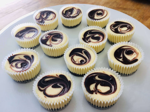 One dozen chocolate ganache cheesecake minis arranged on a white platter, from a side view