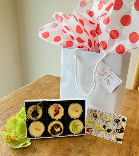 The signature petit gift box standing on a table next to a gift bag and gift tag