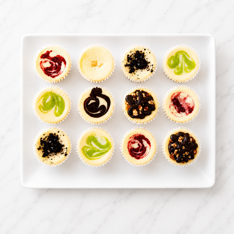 Assorted gourmet cheesecake minis on a white rectangular tray — 12 handcrafted minis in classic, fruit, chocolate, and seasonal flavors from The Cheesecake Boutique, Fayetteville GA. Available for store pickup and Metro Atlanta local delivery.