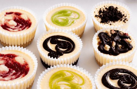 Close-up of Marie's Signature cheesecake minis showing creamy texture, strawberry swirl, key lime, chocolate ganache, and Oreo crumble toppings