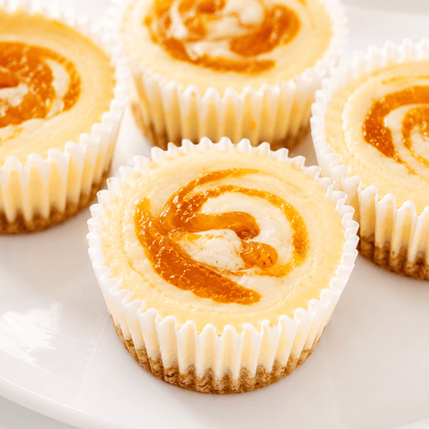 Close-up of Georgia Peaches & Cream cheesecake minis showing creamy filling, golden peach swirl, and buttery citrus-vanilla cookie crust — The Cheesecake Boutique