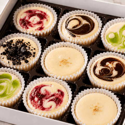 Assorted mini cheesecakes with different flavor swirls of chocolate, strawberry Oreo cookie bits and original in a gift box.