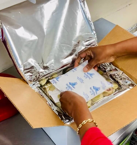 A shipping container being packaged with dry ice, a cheesecake gift box, and a signature collection flavor card.