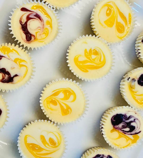 A top down image of Strawberry Lemonade, Blueberry Lemonade, and Luscious Lemon cheesecake minis positioned diagonally on a white plate.