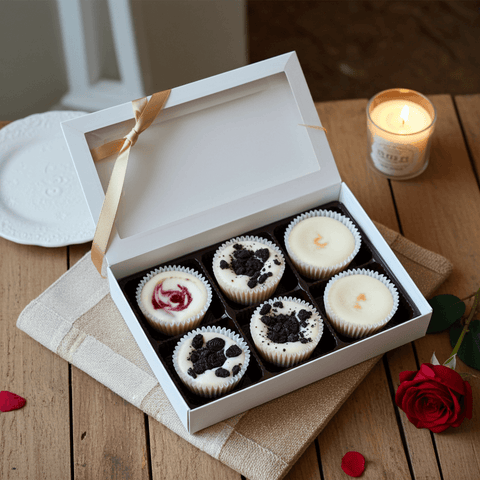 Box of mini cheesecake with a gold ribbon on a wooden table with a lit candle and rose petals.