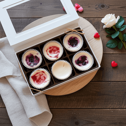 Box of six mini cheesecakes with a heart design on a wooden surface with decorative elements.