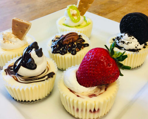 Assorted cupcake-sized cheesecakes with fruit and cookies garnishes on a white plate.
