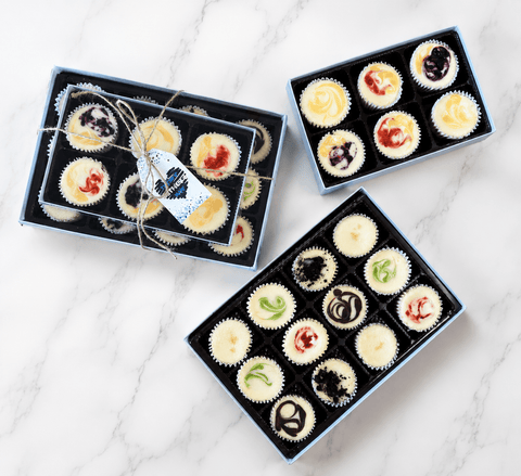 Three gift boxes of assorted mini cheesecakes on a marble surface