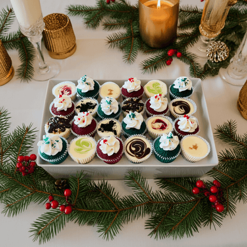 Assorted mini cupcakes and cheesecakes  on a tray with Christmas decorations including candles and greenery.