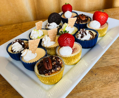 Assorted mini cheesecake dessert cups on a white tray with a wooden table