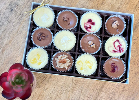A gift box of one dozen assorted chocolate cheesecake minis sitting on a table