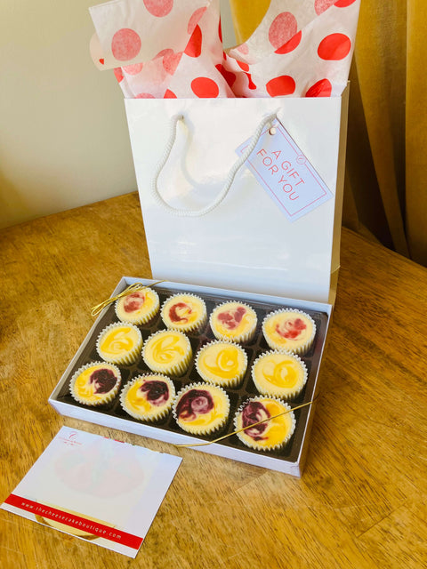 One dozen Spring Flavored mini cheesecakes in a gift box, sitting on front of the glossy tote gift bag and with a personal gift card featuring product details.