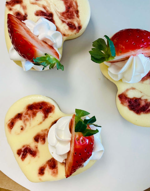 Heart-shaped dessert bites with strawberries and whipped cream on a white surface