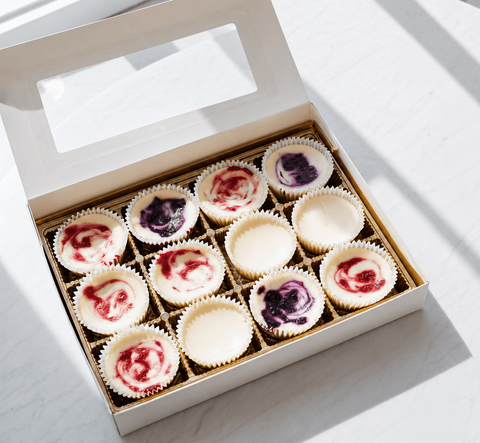 a gift box of twelve assorted mini cheesecakes on a white table