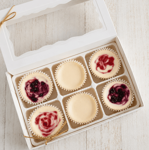 Box of six cheesecake mini cheesecakes with berry swirls on a light wooden surface