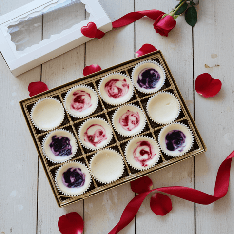 Box of mini cheesecakes with red and purple swirls on a wooden surface with red ribbons and hearts.