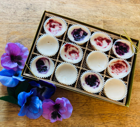 A box of vegan cheesecake bites with swirls of different flavors, presented in a gift box alongside decorative flowers.